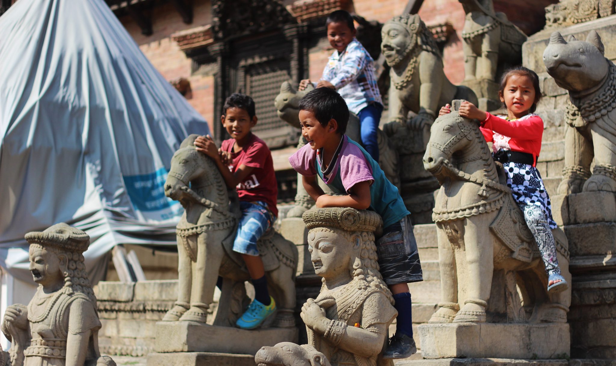 Children play on the stone animals guarding the entrance to the Siddhi Laxmi temple, a 17th-century temple which escaped relatively unscathed from the earthquake.